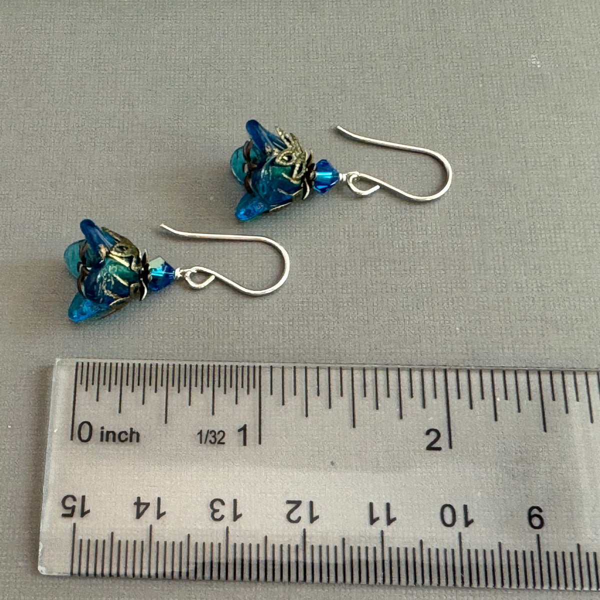 Pair of blue beaded earrings with silver hooks on a gray surface next to a ruler for scale.