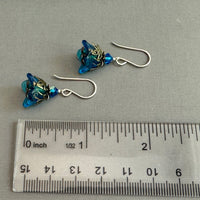 Pair of blue beaded earrings with silver hooks on a gray surface next to a ruler for scale.
