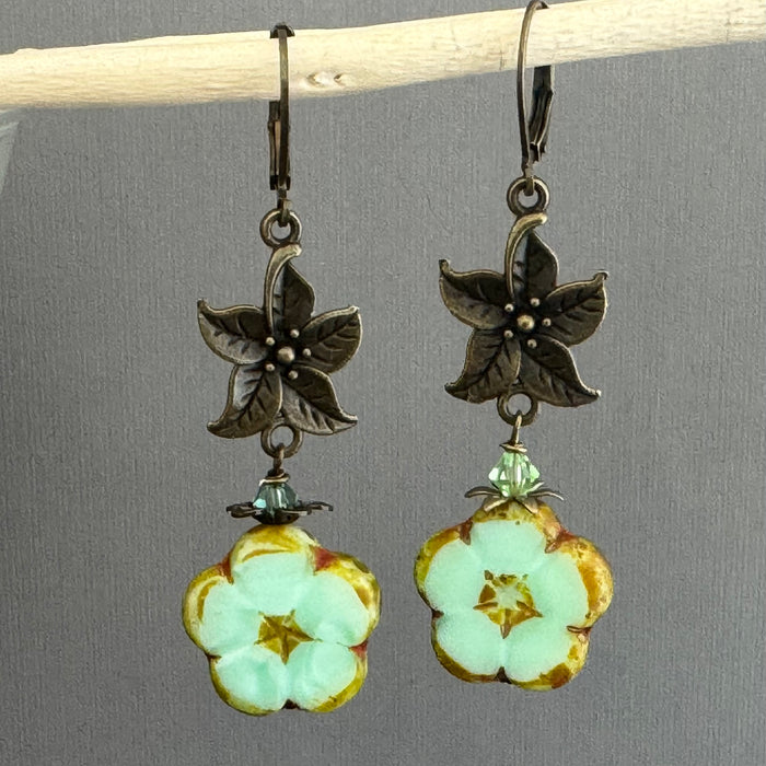 Floral earrings with green and gold flower charms on a gray background