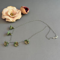 Floral necklace with green flowers on a gray surface next to a silk flower and pod.