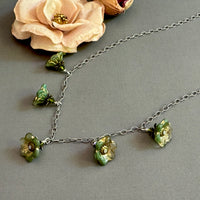Necklace with green floral glass beads on a gray surface with a flower in the background