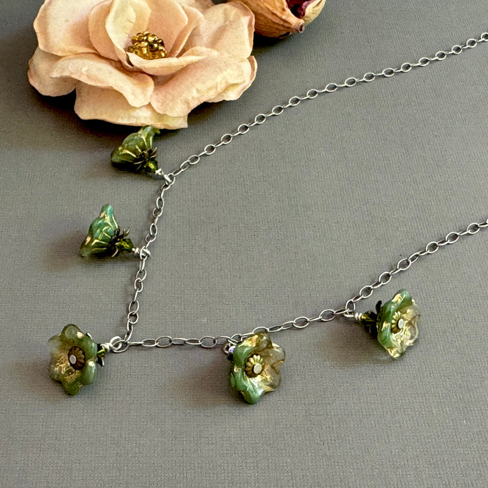Necklace with green floral glass beads on a gray surface with a flower in the background