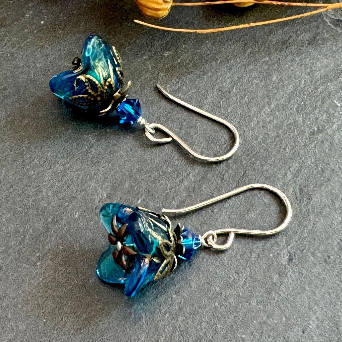 Blue glass flower-shaped earrings on a dark surface.