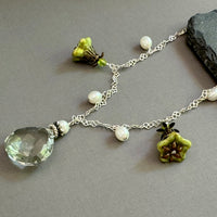 Necklace with green teardrop pendant and floral charms on a gray surface