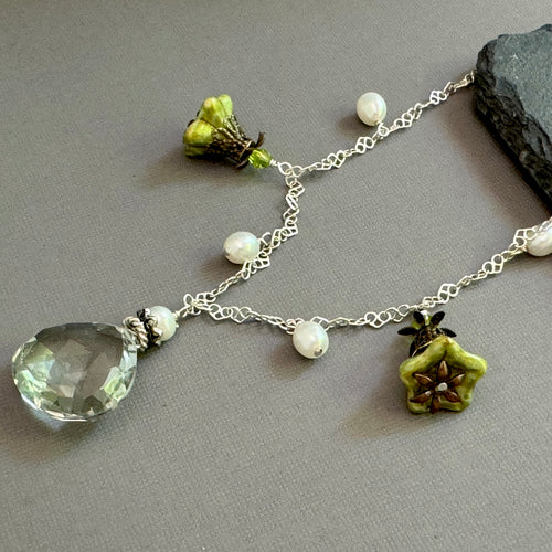 Necklace with green teardrop pendant and floral charms on a gray surface