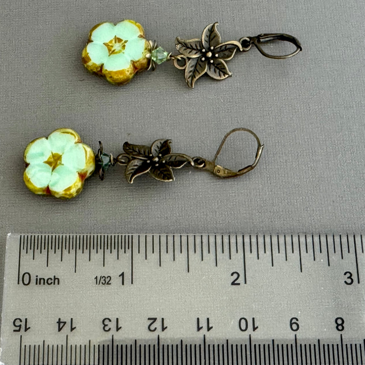 Floral earrings with bronze accents on a gray background, shown with a ruler for scale.