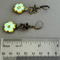 Floral earrings with bronze accents on a gray background, shown with a ruler for scale.